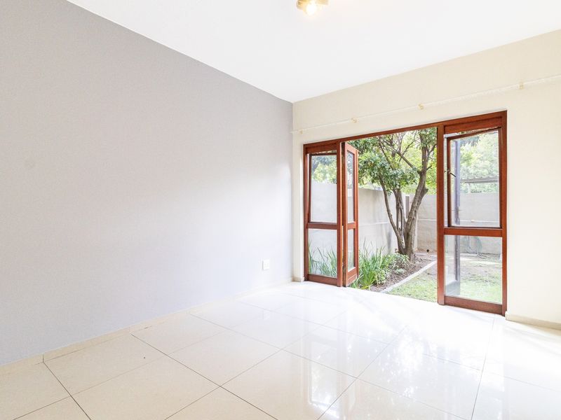 Bright and spacious living area featuring polished tile flooring and large timber-framed glass doors opening directly onto a private garden space.