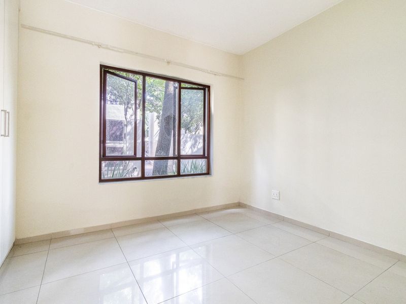 A bright, empty bedroom featuring neutral tiled flooring, a built-in wardrobe, and a large window providing natural light.