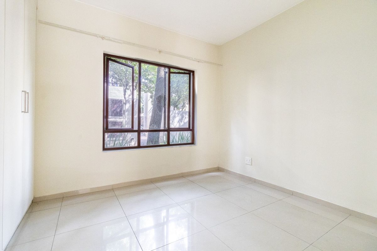 A bright, empty bedroom featuring neutral tiled flooring, a built-in wardrobe, and a large window providing natural light.