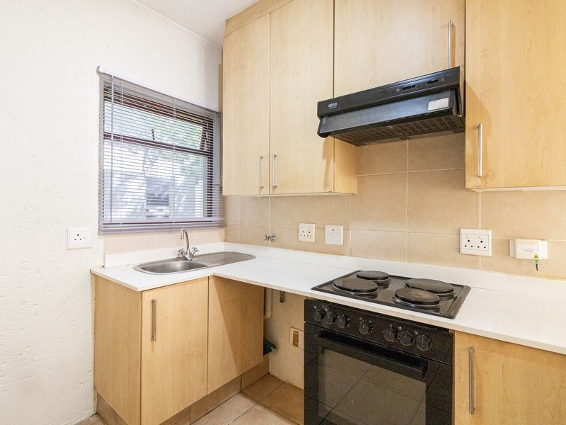 A functional kitchen featuring light wood cabinetry, a built-in oven with hob, extractor fan, and a stainless steel sink with tiled backsplash.