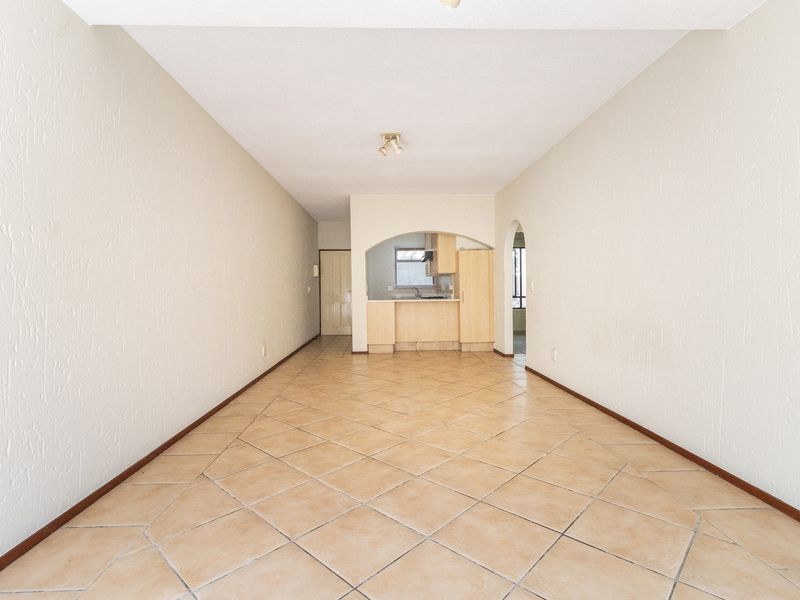 An empty open-plan living and kitchen area featuring neutral tiled flooring, textured walls, and a classic arched entryway leading to the kitchen space.