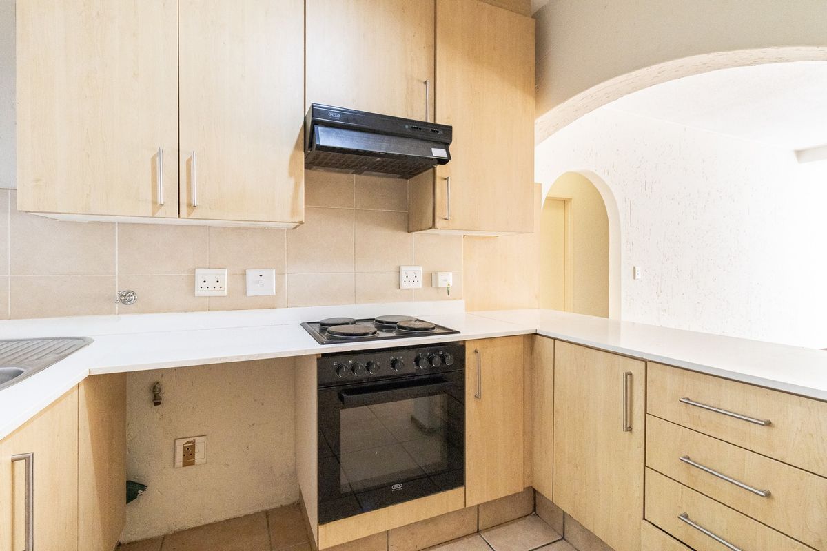 A functional kitchen featuring light wood-finish cabinetry, a built-in oven with hob, extractor fan, and tiled backsplash, leading into an arched hallway.