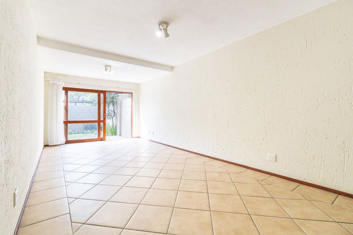 A bright, empty living area featuring neutral tiled flooring, textured walls, and a sliding glass door providing access to the outdoor space.
