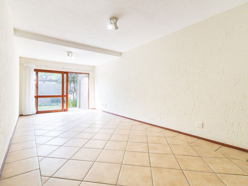 A bright, empty living area featuring neutral tiled flooring, textured walls, and a sliding glass door providing access to the outdoor space.