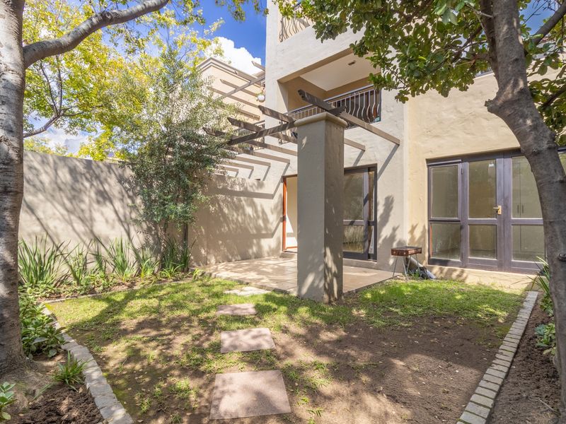 A private rear garden featuring a tiled patio area with a pergola, accessible via sliding glass doors from the apartment.