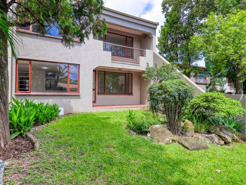 Rear view of the apartment building featuring a ground floor patio, upper-level balcony, and a well-maintained landscaped garden area.
