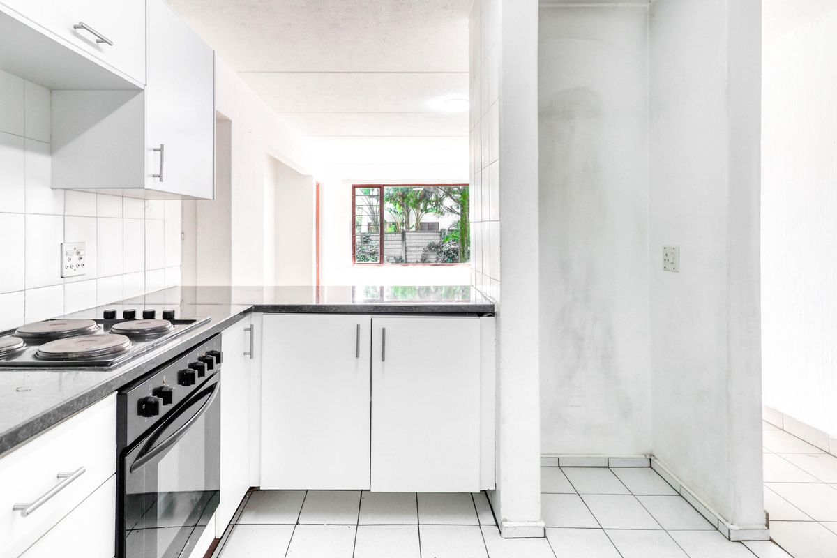 A functional kitchen featuring white cabinetry, a built-in oven with electric hob, tiled flooring, and a tiled backsplash, offering a clean, blank canvas.