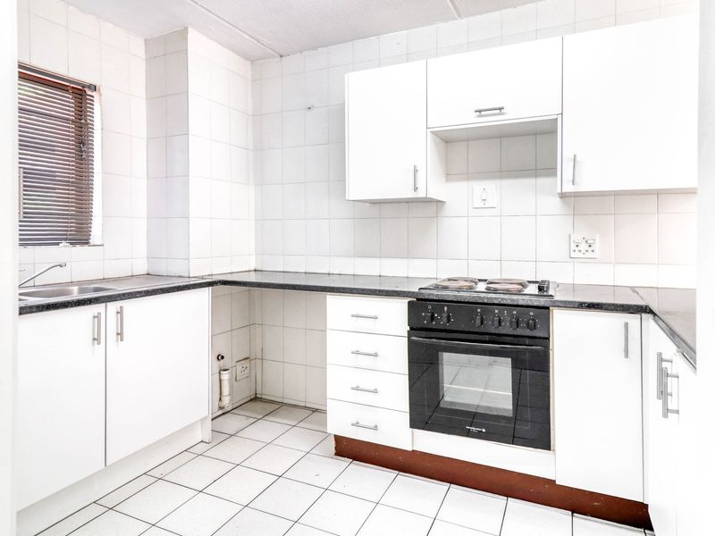 A functional kitchen featuring white cabinetry, dark laminate countertops, a built-in oven with electric hob, and tiled splashbacks.
