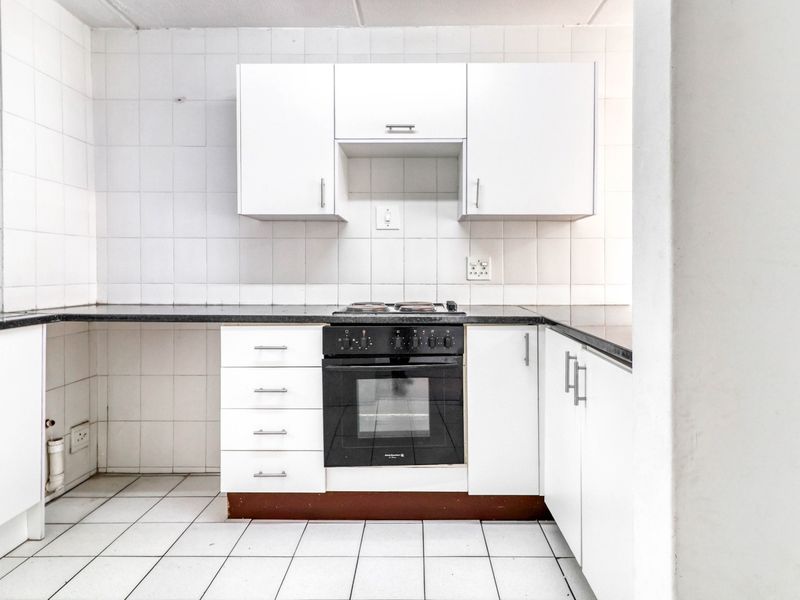 A functional kitchen featuring white cabinetry, black granite countertops, a built-in oven, and a hob, finished with white wall and floor tiles.