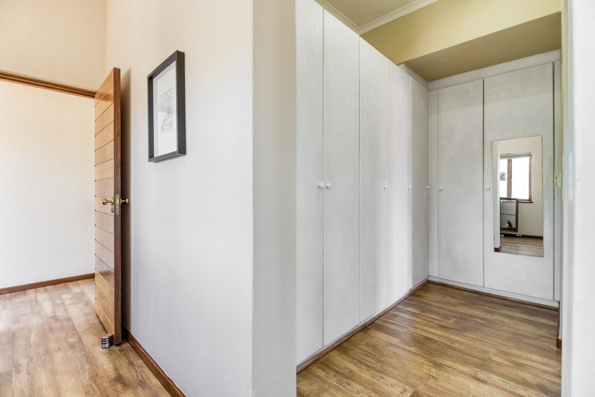 A clean bedroom featuring extensive built-in cupboards, warm laminate flooring, and a solid wooden door, offering a neutral and functional space.