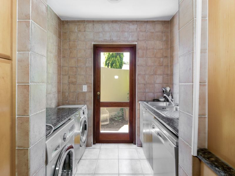 A functional laundry room featuring tiled walls and flooring, granite countertops, a stainless steel sink, and direct access to the exterior.