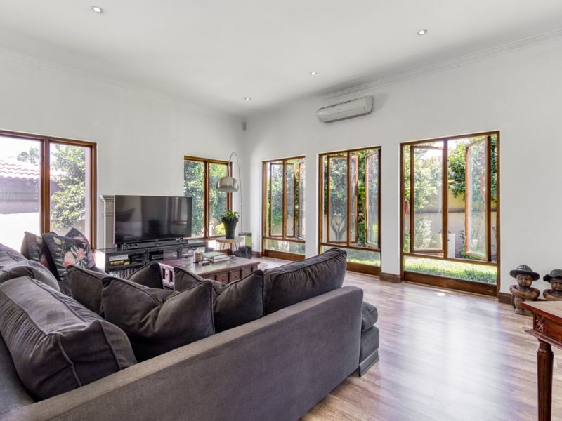 Spacious living room featuring laminate flooring, recessed downlighting, and multiple timber-framed casement windows providing natural light and garden views.