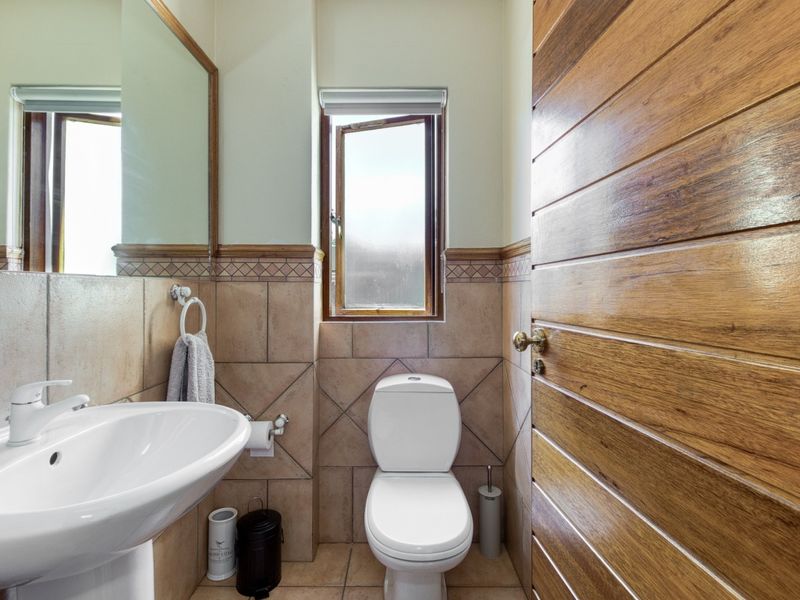 A compact bathroom featuring a pedestal washbasin, toilet, tiled finishes, and a wooden door, providing a functional and well-maintained space.