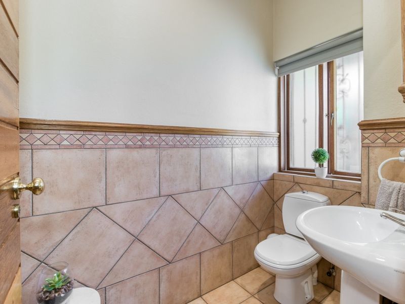 A compact guest bathroom featuring tiled wall accents, a pedestal basin, and a toilet, with natural light provided by a timber-framed window.