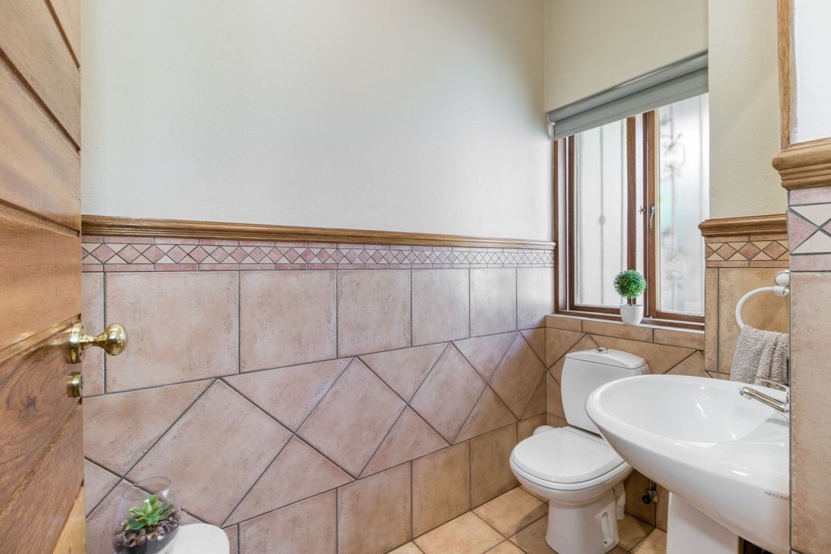 A compact guest bathroom featuring tiled wall accents, a pedestal basin, and a toilet, with natural light provided by a timber-framed window.