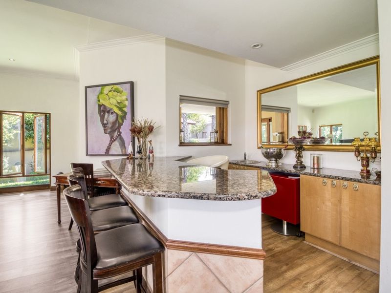 A well-appointed home bar area featuring a granite-topped counter, built-in cabinetry, an integrated sink, and a large wall mirror.
