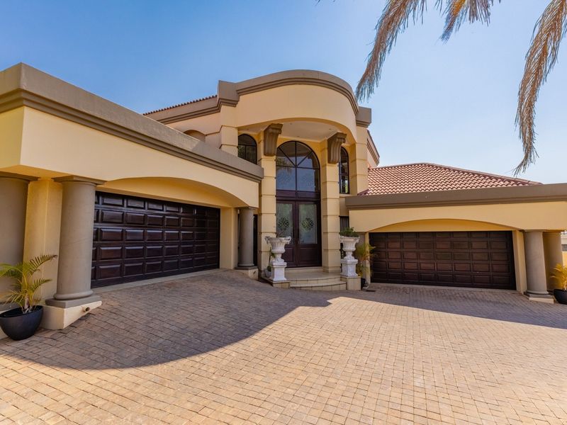 A well-maintained front elevation featuring a paved driveway, double garage, and an impressive arched entrance with decorative columns.