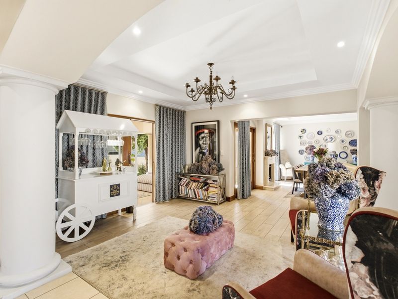Spacious living area featuring elegant decorative columns, a recessed ceiling with cove lighting, and tiled flooring, flowing into an adjacent dining space with a fireplace.
