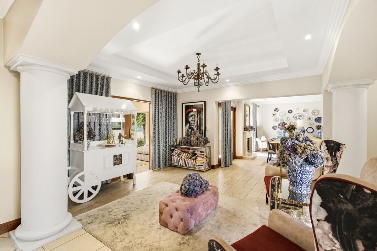 Spacious living area featuring elegant decorative columns, a recessed ceiling with cove lighting, and tiled flooring, flowing into an adjacent dining space with a fireplace.