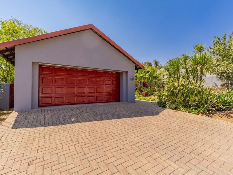 A well-maintained detached garage featuring a red sectional door, paved driveway, and established garden surroundings.