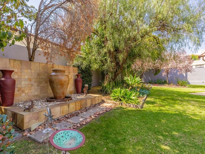 A well-maintained garden featuring a stone-tiled water feature, established trees, landscaped garden beds, and a lush green lawn.