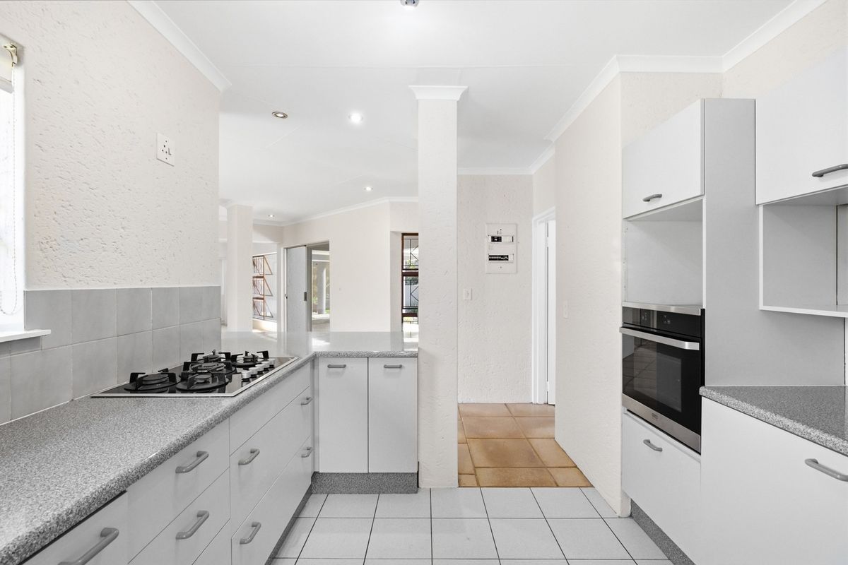 A clean, functional kitchen featuring white built-in cabinetry, granite countertops, a gas hob, and a built-in oven with tiled flooring throughout.