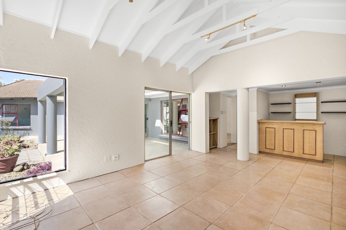 Spacious living area featuring a vaulted ceiling with exposed rafters, tiled flooring, and a built-in bar, opening out to an outdoor patio area.
