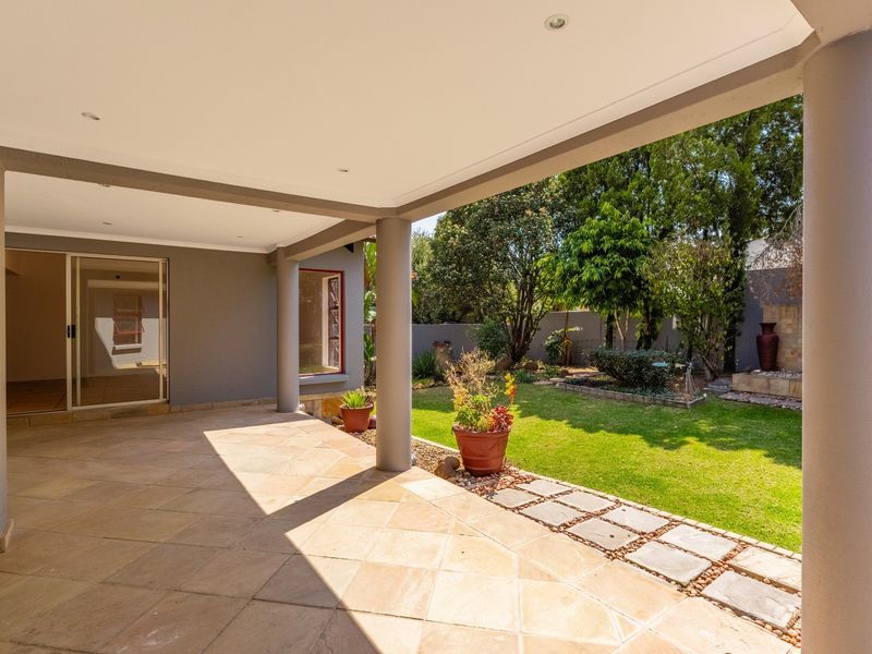 A spacious covered patio featuring tiled flooring and recessed lighting, overlooking a well-maintained private garden with a stone pathway.
