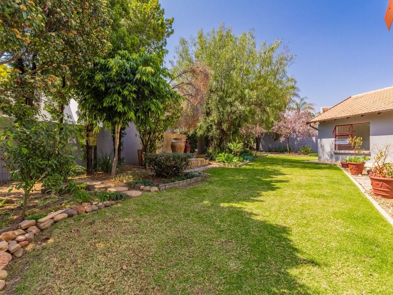 A well-maintained rear garden featuring a lush lawn, mature trees, stone-edged garden beds, and a view of the property's exterior facade.