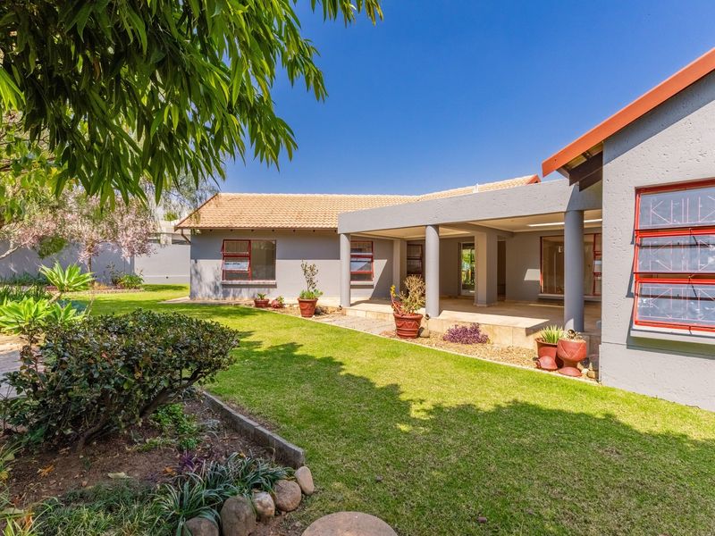 A well-maintained rear exterior view featuring a covered patio, landscaped garden, and classic tiled roof architecture.