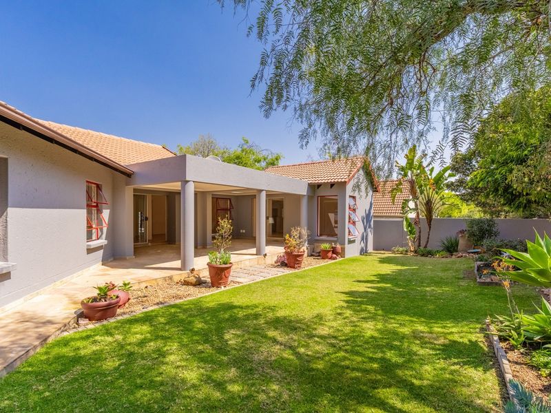 A well-maintained rear exterior view featuring a covered patio, paved walkway, and a landscaped garden with a boundary wall.