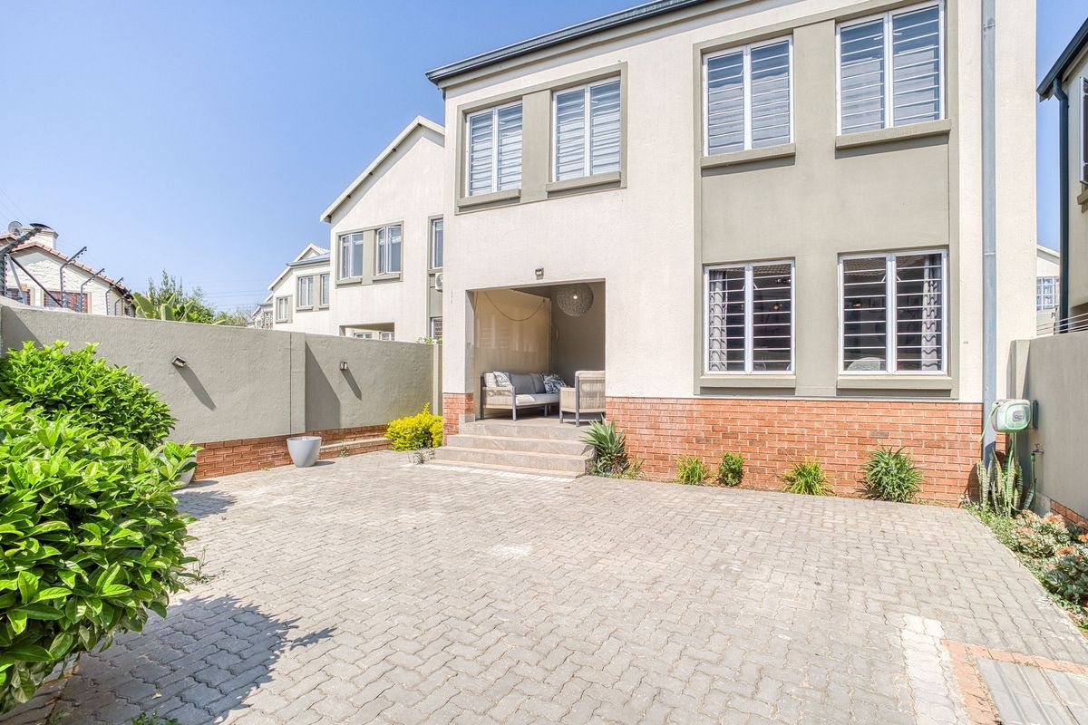 Rear view of the property featuring a paved courtyard, brick boundary wall, and a covered patio area with access to the main building.