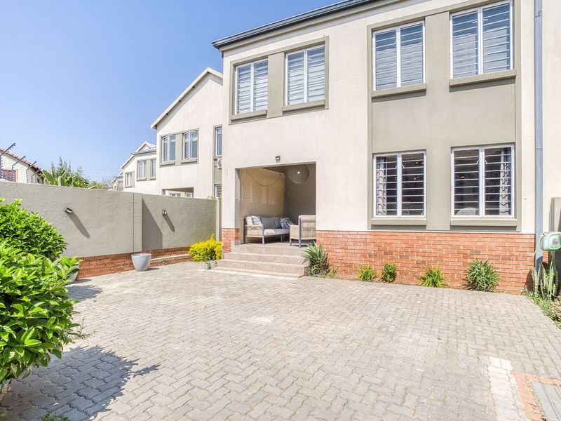 Rear view of the property featuring a paved courtyard, brick boundary wall, and a covered patio area with access to the main building.