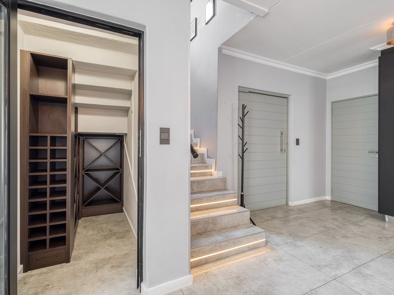 Modern entrance hall featuring tiled flooring, a staircase with integrated LED lighting, and a dedicated built-in wine storage area under the stairs.