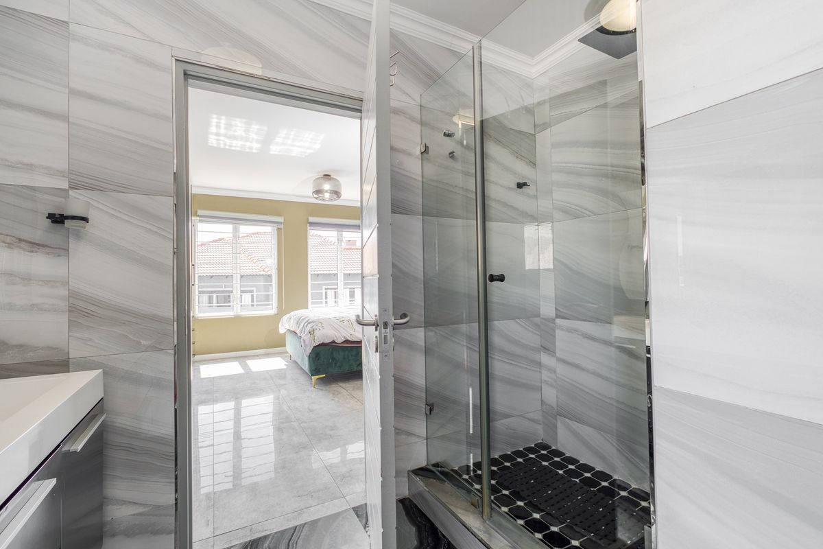 Modern bathroom featuring a glass-enclosed shower, marble-look wall tiles, and a sleek vanity, with direct access to the adjacent bedroom.