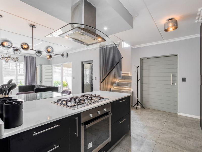 Modern open-plan kitchen featuring a central island with gas hob, built-in oven, sleek cabinetry, and a stylish staircase with integrated lighting.