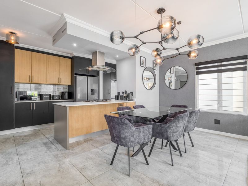 Modern open-plan kitchen and dining area featuring contemporary two-tone cabinetry, stone countertops, high-end integrated appliances, and stylish feature lighting.