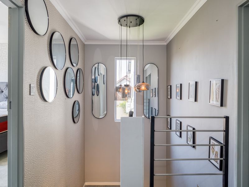 A well-lit hallway featuring a modern staircase railing, decorative pendant lighting, and textured wallpaper, providing access to adjacent bedrooms.