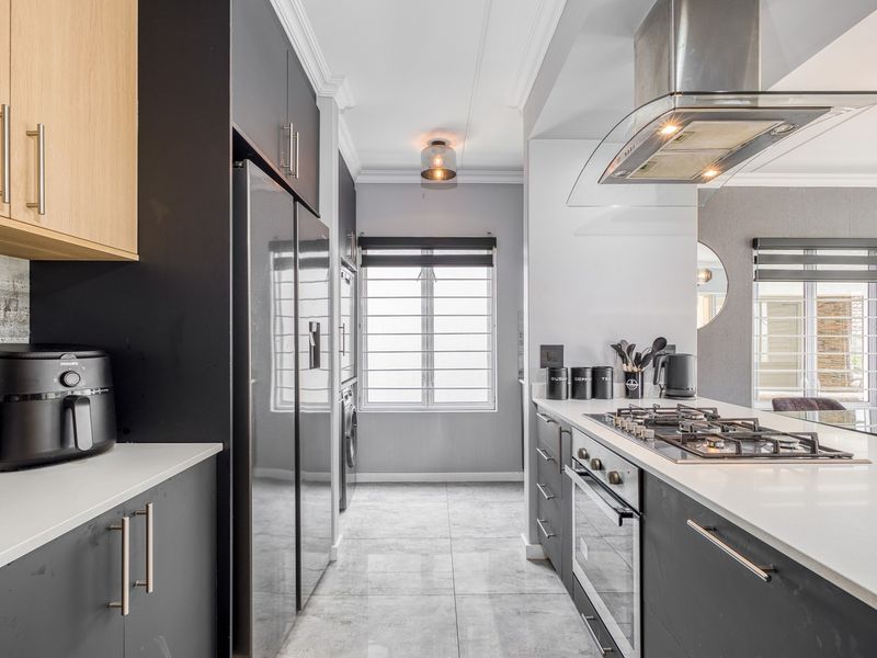 Modern kitchen featuring sleek dark cabinetry, quartz countertops, a gas hob, built-in oven, and high-quality stainless steel extractor fan.