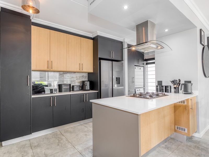 Modern kitchen featuring two-tone cabinetry, stone countertops, a central island with a gas hob, and high-quality stainless steel extractor fan.