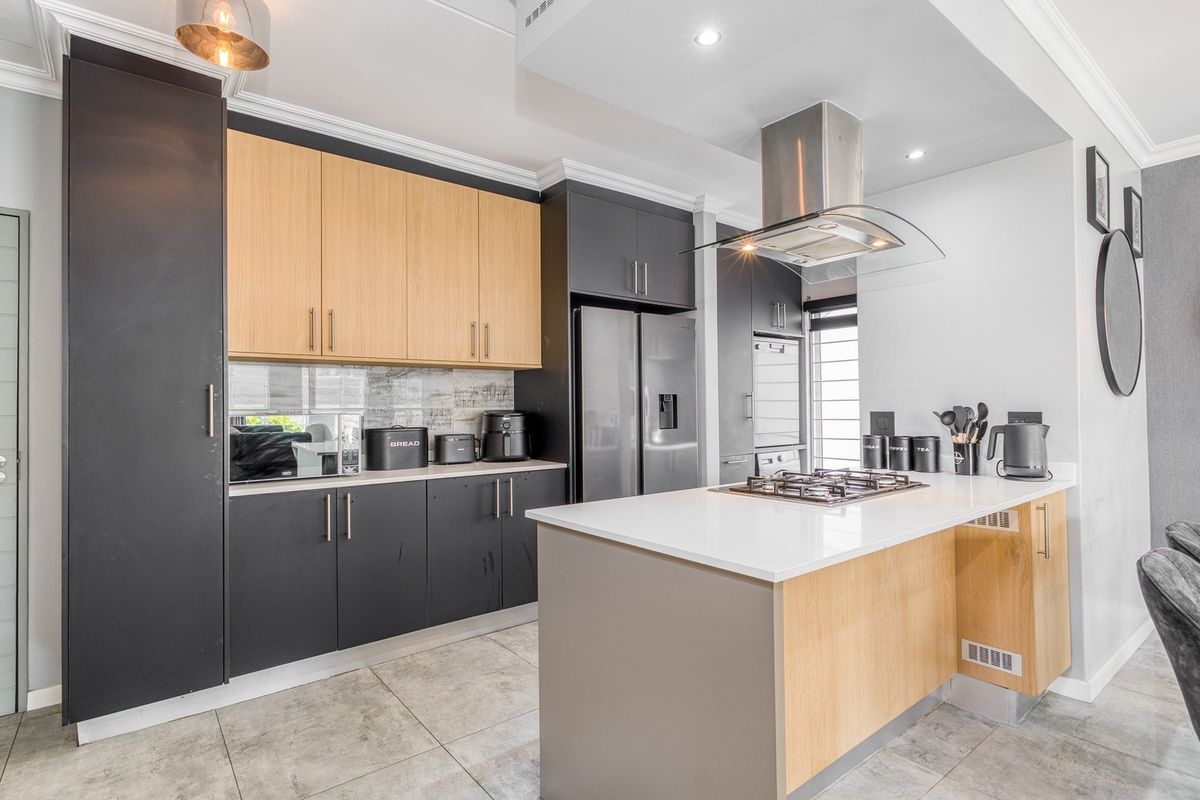 Modern kitchen featuring two-tone cabinetry, stone countertops, a central island with a gas hob, and high-quality stainless steel extractor fan.