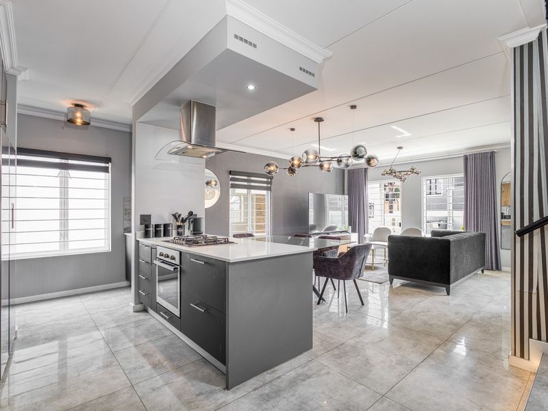 Modern open-plan living area featuring a sleek kitchen island with built-in oven and hob, complemented by polished porcelain flooring and contemporary lighting.
