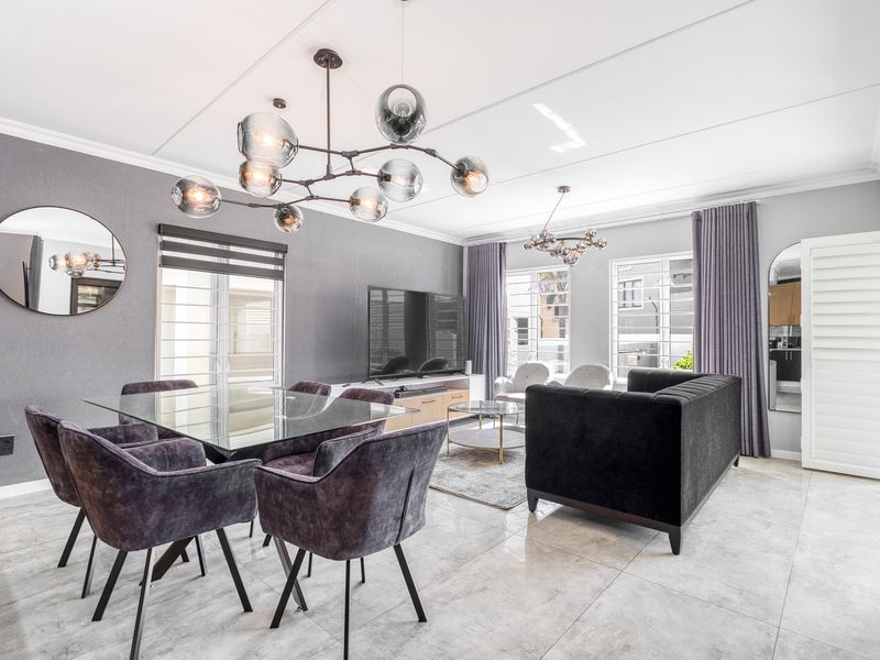 A bright and modern open-plan living and dining area featuring large format floor tiles, contemporary lighting fixtures, and neutral grey wall finishes.