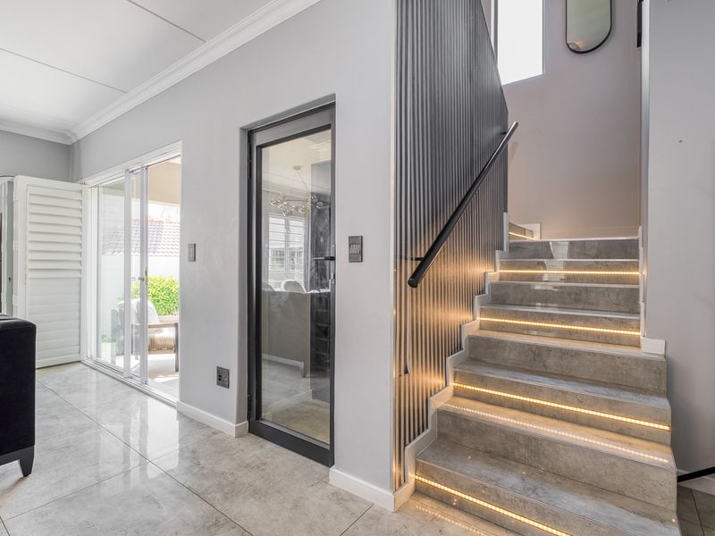 Modern hallway featuring a contemporary staircase with integrated LED lighting, slatted wall detailing, and glass doors leading to an outdoor patio area.