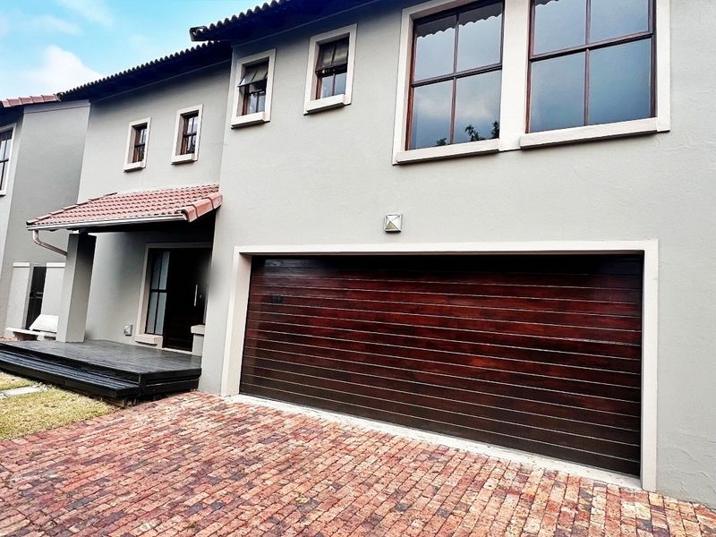 Front elevation of a double-story house featuring a dark timber garage door, brick paved driveway, and a covered entrance with timber decking.