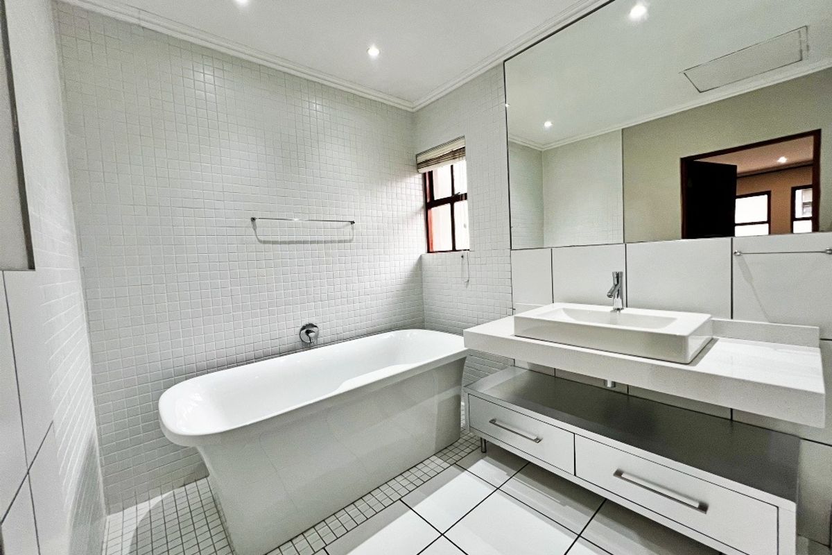 Modern bathroom featuring a sleek freestanding bathtub, floating vanity with a vessel sink, large wall mirror, and clean white tiled finishes.