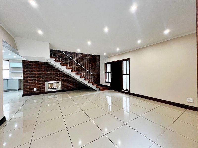 Spacious open-plan living area featuring polished tile flooring, an exposed brick feature wall with a built-in fireplace, and a modern staircase.