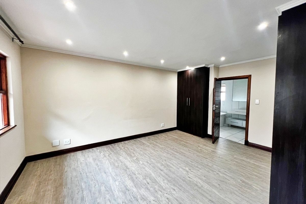 Spacious bedroom featuring modern laminate flooring, built-in cupboards, recessed downlighting, and direct access to an en-suite bathroom.