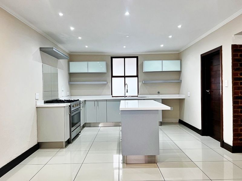 Modern kitchen featuring a central island, gas stove, extractor fan, quartz countertops, and sleek cabinetry with recessed lighting and tiled flooring.
