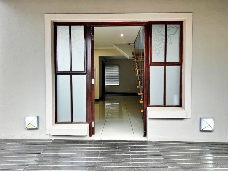A modern entrance featuring a timber deck, frosted glass door, and a view into the tiled interior with a floating staircase.